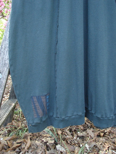 Barclay Patched Thermal Curve Dress Forest Size 2: A dark-colored dress with a unique figure-eight shape, featuring a mesh panel near the hem, hanging outdoors against a rustic backdrop.