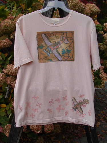 2001 Short Sleeved Tee Airplane Pink Tile Size 0: A pink shirt with a picture of airplanes on it, made from mid-weight organic cotton. Slightly thicker ribbed neckline, drop shoulders, and slightly longer length. Bust 48, waist 48, hips 48, length 28 inches.