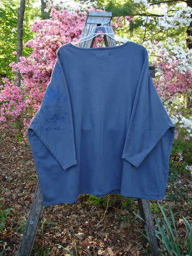 Barclay Fleece Big Square Pullover Botanical Path Night Navy OSFA, displayed on a wooden ladder outdoors, features dolman shoulders, cozy sleeves, and a square A-line shape amidst a backdrop of flowering shrubs.