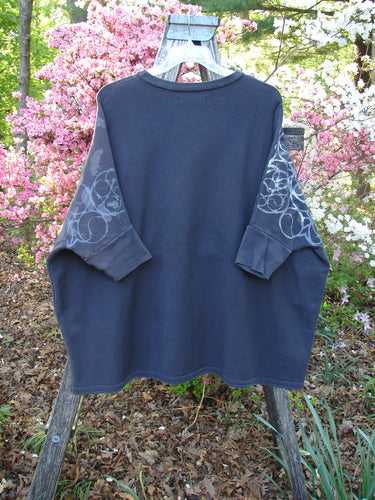 Barclay Fleece Banded Sleeve Dolman Top Continuous Spirograph Black OSFA displayed on a wooden trellis, featuring circular patterns on sleeves, wide boxy shape, and banded hem against a floral background.