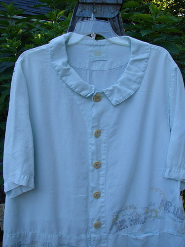 2000 Tencel Camp Shirt Airmail Shark Size 0 displayed on a hanger, showcasing its smaller Peter Pan collar, oversized contrasting buttons, front drop pocket, and flowing, light fabric with a travel airmail theme.