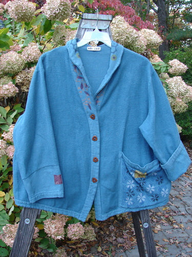 A Barclay Patched Flannel Frolic Jacket in Ocean Teal with a garden-themed exterior pocket, contrasting lower sleeves, and unique buttons.