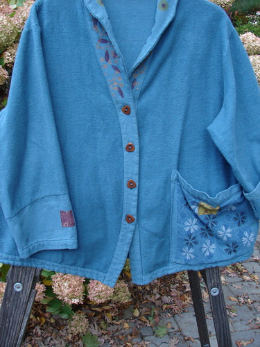 A Barclay Patched Flannel Frolic Jacket in Ocean Teal with a garden-themed exterior pocket, contrasting lower sleeves, and unique buttons.