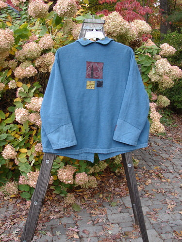 A blue Barclay Patched Flannel Frolic Jacket with garden-themed patches and unique buttons, swinging on a wooden swinger.