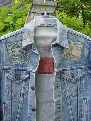1995 Patched Levi Strauss & Co Denim Blue Jean Jacket Kitty Kitty Stone Wash Size 0 displayed on a hanger, featuring hand-sewn patches with abstract motifs, highlighting its vintage craftsmanship and unique artistic details.