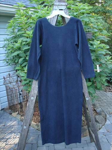 A blue long-sleeved dress, titled 1991 Rib Thermal The Skinny Dress Unpainted Charcoal Altered OSFA, draped on a wooden ladder. The dress features a straight linear shape and a rounded neckline.