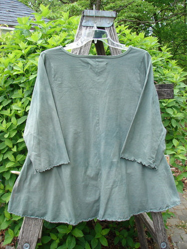 Barclay Crop A Lined Cafe Tee Cow Farm Grass Size 0, featuring a slightly flared silhouette with a rounded neckline and curly edgings, displayed on a wooden step-ladder against a verdant backdrop.