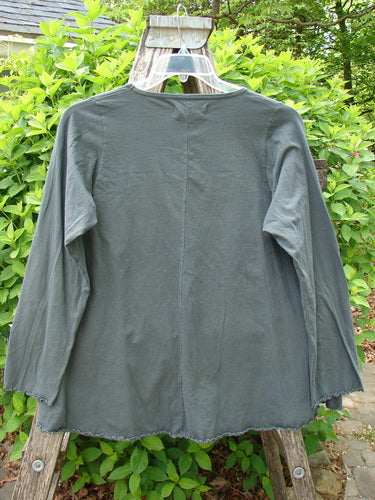 Barclay Long Sleeved Cafe Tee Love Dove Home Grey Hunter Size 0 showcased outdoors with scalloped edges, hanging on a wooden structure amid green foliage, highlighting its organic cotton fabric and unadorned back design.