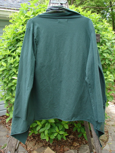 Barclay Cotton Lycra Gather Collar Open Front Jacket Golden Forest Size 0 hangs on a wooden rack, showcasing its drape-front design, unique drawcord neckline, and long sleeves against a leafy backdrop.