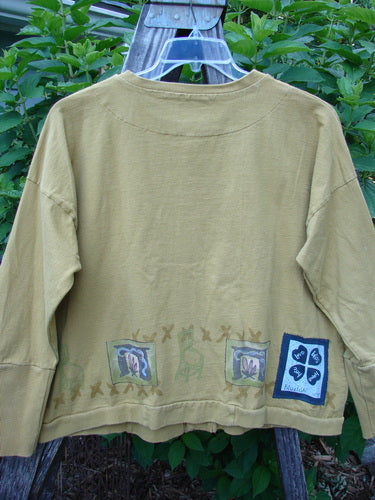 1999 Cottage Cardigan Campfire Gold Size 1 displayed on a hanger, featuring ribbed lower sleeves, double-layered neckline, hemline, and front pocket, with oversized vintage buttons and signature Blue Fish patch.