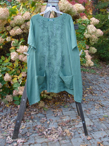 Barclay Linen Two Pocket Curve Dress featuring Botanical Vine design in Fresh Moss, Size 2, on a wooden stand. Unique curvy seams, art front panel, drop pockets, A-line shape, and wide sleeves. Vintage Blue Fish Clothing at BlueFishFinder.com.