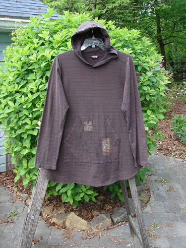 Barclay Cotton Lycra Twinkle Hoodie Pullover Geisha Stripe Bark Size 0 draped on a wooden ladder, showcasing its kangaroo pocket with decorative patches and clear-lens goggles tucked inside the hood.