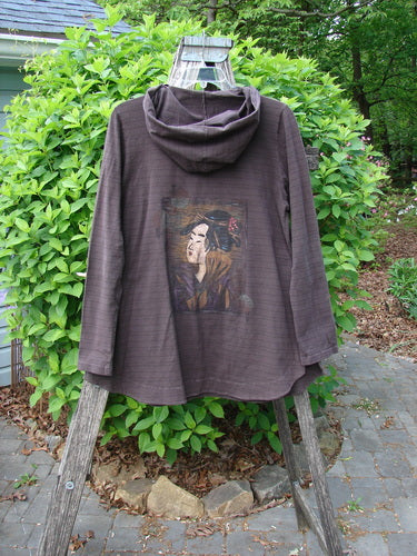 Barclay Cotton Lycra Twinkle Hoodie Pullover Geisha Stripe Bark Size 0 draped over a wooden ladder, showcasing its cozy hood, portrait print, and wide kangaroo pocket, set against a leafy backdrop.