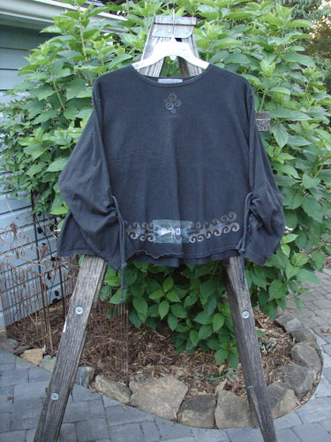 1997 Chandra Top Celtic Holiday Obsidian Size 1 displayed on a wooden ladder, showcasing full lower sleeve lacings, wide hemline, rolled neckline, continuous Celtic holiday theme paint, and a drawcord back.