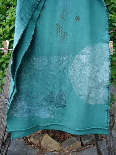 Barclay Heavy Weight Organic Sweatshirt Art Wrap Moon Garden Emerald OSFA draped on a wooden bench outdoors, featuring mandala and abstract motifs, clipped with wooden clothespins amidst garden foliage.