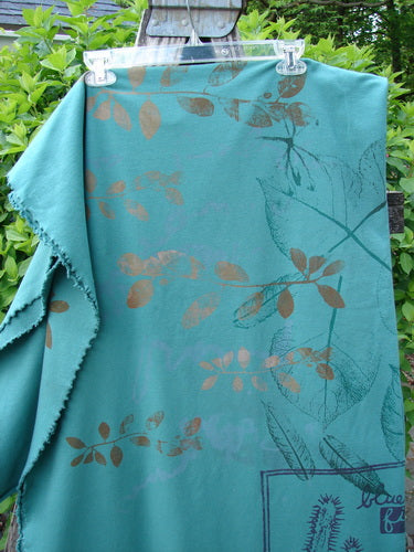Barclay Heavy Weight Organic Sweatshirt Blanket Pony Garden Emerald OSFA, draped on a hanger, features a botanical motif with leaf silhouettes and raw curly edges, showcasing a versatile and artistic design.