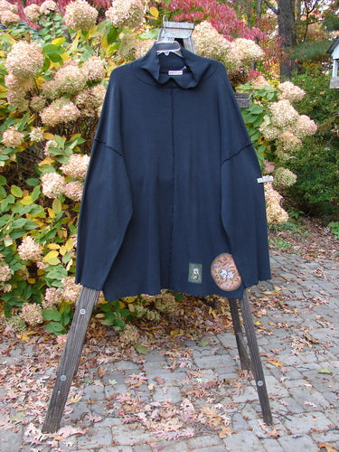 A black tunic with nature-themed painted patches, floppy turtleneck, and unique square shape.