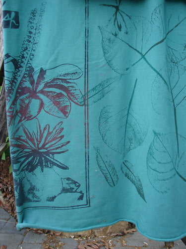Barclay Heavy Weight Organic Sweatshirt Blanket Pony Garden Emerald OSFA hangs outdoors, showcasing a botanical motif with large leaves and flowers, featuring raw cut edges and a unique, versatile design.