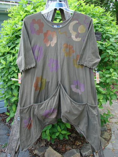 Barclay Quad Pocket Tie Back Tunic Dress in Simple Floral Mushroom, featuring elbow-length sleeves, scooped neckline, and quad drop pockets, displayed outdoors against green shrubs.