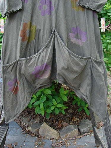 Barclay Quad Pocket Tie Back Tunic Dress in Mushroom, features a loose-fitting design with abstract floral patterns, oversized patch pockets, and a rounded neckline, hanging outdoors on a wooden rack.