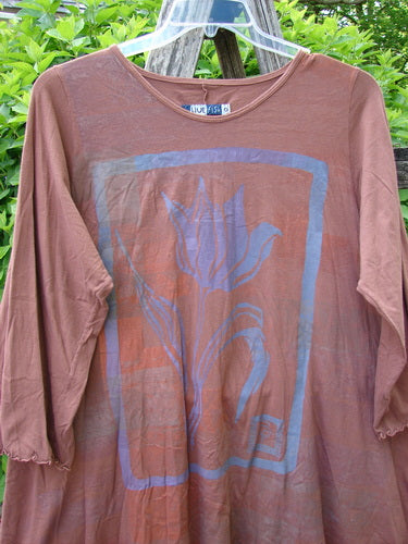 Barclay Three Quarter Sleeve Color Wheel Tunic Tulip Gourd Size 0, featuring a stylized tulip print on rust-brown organic cotton, with a rounded neckline and lettuce-edged sleeves, hanging outdoors.