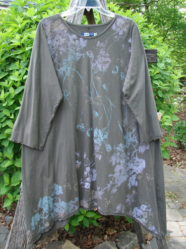 Barclay Three Quarter Sleeve Color Wheel Tunic Falling Floral Black Sand Size 0: Olive-gray tunic with asymmetrical hemline, blue floral print, and lettuce-edged sleeves, hanging on a clear plastic hanger outdoors.