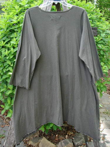 Barclay Three Quarter Sleeve Color Wheel Tunic Falling Floral Black Sand Size 0, featuring an uneven hemline, rounded neckline, and three-quarter lettuce-edged sleeves, displayed against green shrubbery.