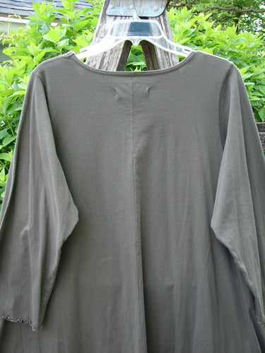 Barclay Three Quarter Sleeve Color Wheel Tunic Falling Floral Black Sand Size 0, featuring a loose fit, rounded neckline, and three-quarter lettuce-edged sleeves, displayed outdoors against leafy shrubs on a hanger.