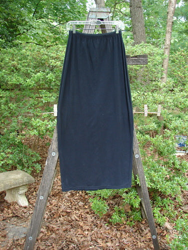 1995 Cotton Lycra Column Skirt Unpainted Black Tiny Size 2 displayed on a wooden ladder outdoors, showcasing its full elastic waistline, tapering shape, and pegged hemline.