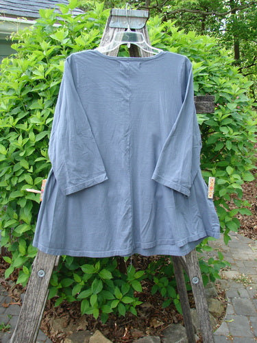 Barclay Three Quarter Sleeved A Lined Tee Wandering Dust Plum Size 0, displayed on a wooden ladder with leafy shrubbery backdrop, showcasing its loose fit, rounded neckline, and curly edgings.