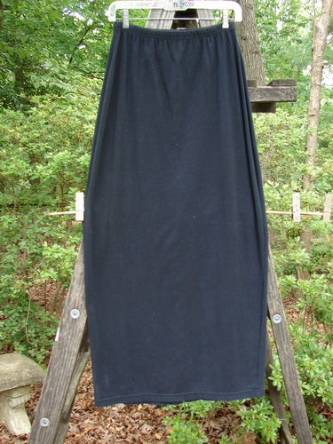 Alt text: 1995 Cotton Lycra Column Skirt Unpainted Black Tiny Size 2, displayed hanging from a wooden ladder, showcasing its tapered shape and full elastic waistline.