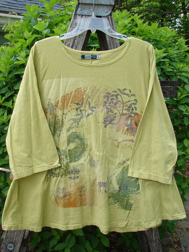 Barclay Three Quarter Sleeved A Lined Tee Field Friend Citron Size 0, featuring a loose fit, overlapping color blocks with flora and fauna motifs, displayed on a hanger against a leafy backdrop.