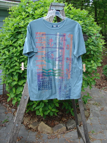 Barclay Short Sleeved Straight Tee BF Promo Light Tealen Size 0, featuring a stylized fish graphic and wavy lines, hangs on a wooden trestle with a natural backdrop, showcasing its relaxed, artistic design.