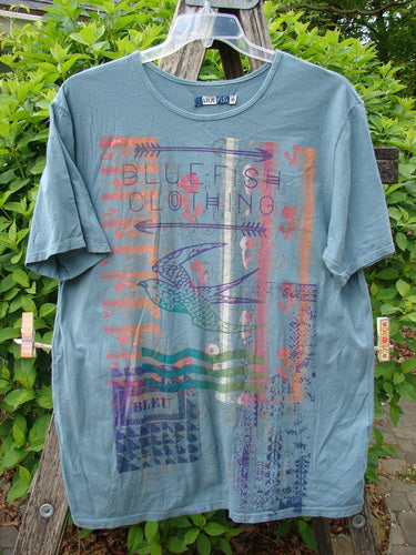 Barclay Short Sleeved Straight Tee BF Promo Light Tealen Size 0, featuring a vibrant multicolored graphic with stylized bird and geometric patterns, hangs outdoors, showcasing its relaxed fit and organic cotton texture.