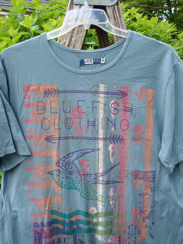 Barclay Short Sleeved Straight Tee BF Promo Light Tealen Size 0 features a multicolored graphic with BLUE FISH CLOTHING text and a stylized swallow, hanging outdoors against green foliage.