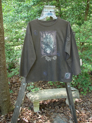 1994 Long Sleeved Tee Forest Leaf Humus Size 1 displayed on a ladder, showcasing drop shoulders, ribbed neckline, and unique forest leaf theme paint with iron gate detail. Vintage Blue Fish Clothing.