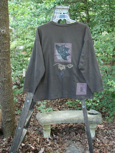 Alt text: 1994 Long Sleeved Tee Forest Leaf Humus Size 1 displayed on a wooden ladder, showcasing its ribbed neckline, drop shoulders, and signature forest leaf theme paint.