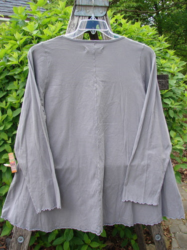 Barclay Long Sleeved Cafe Tee Poetry Garden Grey Day Size 0, featuring scalloped edges and a flared cut, elegantly displayed on a hanger with lush greenery backdrop, highlighting its unique style.