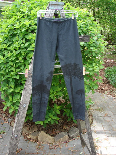 Barclay Cotton Lycra Relaxed Legging Shadow Tree Lux Silhouette Size 0, featuring tree silhouettes on lower legs, hangs on a wooden step-ladder outdoors, showcasing its elastic waistband and forgiving fit.