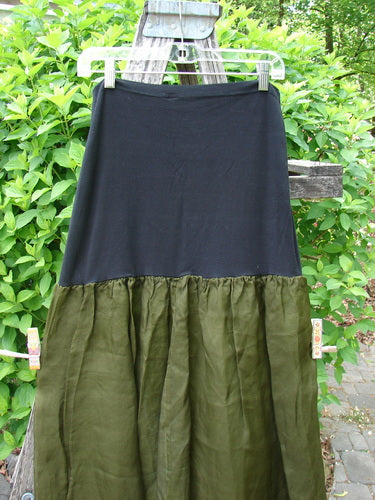 2000 Silk Organza Aios Dana Skirt Celtic Lichen Size 1, featuring a black lycra upper and an olive-green flared lower section, elegantly displayed against a leafy backyard backdrop.