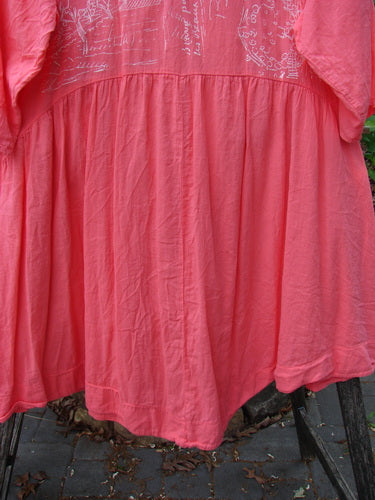 Barclay Linen Two Pocket Dolly Dress Notes Coral Size 0, featuring white doodle designs on the upper part, a flouncy lower skirt, and dual exterior drop pockets, displayed hanging outdoors.
