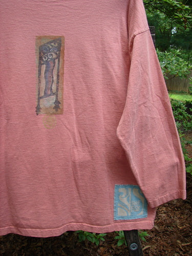 Alt text: 1995 Long Sleeved Tee Vintage Column Papaya Size 1 featuring a painted design of a man holding a pole, thicker ribbed neckline, drop shoulders, and Blue Fish signature patch.