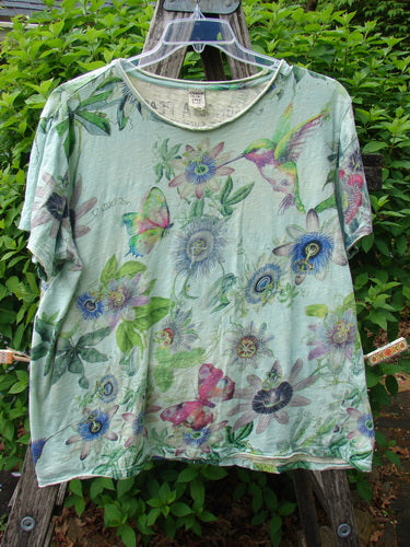 Magnolia Pearl Cotton Jersey Boyfriend Tee Passion Flower Big Sky OSFA, featuring a drapey, loose fit with a watercolor botanical motif of flowers and hummingbirds, displayed on a wooden trellis outdoors.