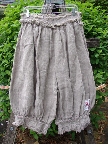 Magnolia Pearl Homespun Linen Crop Smocked Bloomer Flaxen OSFA hanging outdoors on a clip hanger, showing its vintage-inspired design with a full smocked waistline, ruffled cuffs, and signature patches.