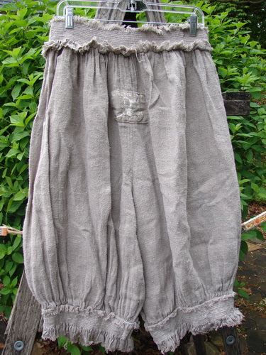 Magnolia Pearl Homespun Linen Crop Smocked Bloomer, featuring a ruffled elastic waist and cuffs, billowy knee-length design, with distinctive Magnolia Pearl patches, hanging outdoors on a metal hanger.