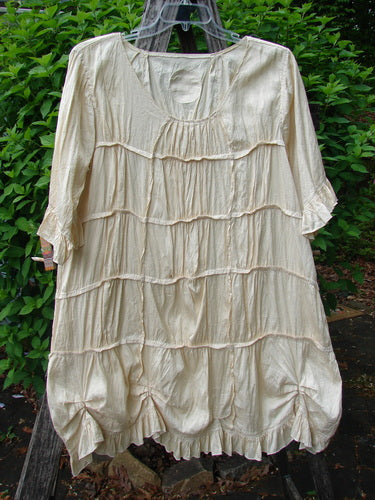 The Magnolia Pearl Silk Cotton Drapery Dress Butter Creme OSFA features a scooped neckline, elbow-length sleeves, and horizontal ruffles, embodying vintage charm with its gathered hem and tiered front design.