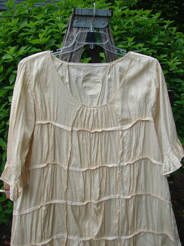 Magnolia Pearl Silk Cotton Drapery Dress Butter Creme OSFA on hanger, showcasing oval neckline, fluttery sleeves, tiered layers, and full ruffled hem against leafy backdrop, embodying Bluefishfinder.com's vintage elegance.