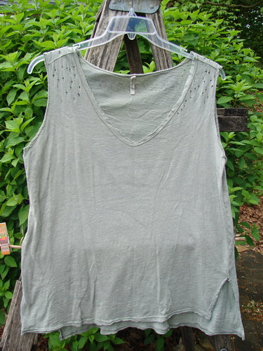 Magnolia Pearl Cotton Jersey Vented Layer Tank Top Green River OSFA hangs on a wooden ladder outdoors, showcasing its wide V-neck, vented sides, raw flutter edges, and unique distressing details.