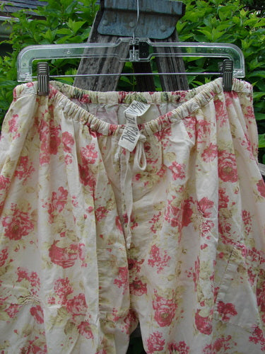 Magnolia Pearl Patched Khloe Bloomer Roses Are Red OSFA pants with pink and green floral print, elastic waist with drawstring, scallop tape hems, and hand-mended rose garden patches, hanging on a clear hanger.