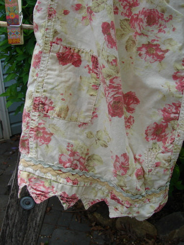 Magnolia Pearl Patched Khloe Bloomer Roses Are Red OSFA, featuring pink and red roses on cream. Details include raw-edge pocket, rickrack trim, scalloped hem, and a distressed fabric finish, embodying vintage charm.